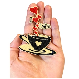 Può includere: Toppa ricamata da stirare con una tazza di caffè nera con un cuore bianco e un vapore di cuori rossi che dice "Amo il caffè".
