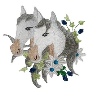 May include: Embroidered patch featuring two white horses with brown manes and tails, surrounded by white flowers with blue centres and green leaves with blue berries.