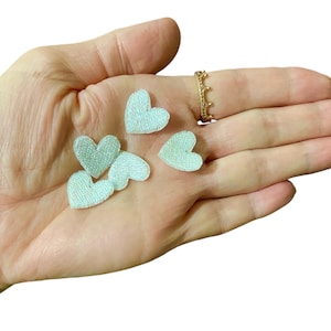 Peut inclure: Une main tenant plusieurs petits patchs en forme de cœur en feutre bleu clair.