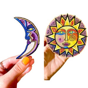 Op de afbeelding: Twee geborduurde strijkpatches, een met een halve maan met een gezicht en de andere met een zon met een gezicht. De maan is paars, blauw en wit, terwijl de zon geel, oranje, rood en roze is.