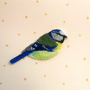 May include: Embroidered bluebird patch with a blue, green, and yellow design. The bird is facing right and has a small, pointed beak.
