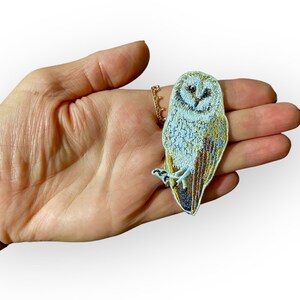 May include: A white and brown embroidered iron-on patch of a barn owl with a light blue background.