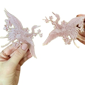 May include: Two pink embroidered iron-on patches of cranes with floral accents.