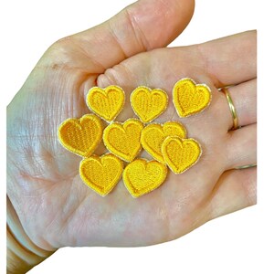 Könnte beinhalten: Zehn kleine gelbe Filzherzen-Patches. Die Herzen sind etwa 2,5 cm groß und haben einen weißen Umriss.