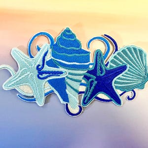 Puede incluir: Parche bordado con una concha, dos estrellas de mar y una concha de vieira en tonos azules y blancos. El parche tiene un diseño detallado con un borde blanco y está sobre un fondo degradado.