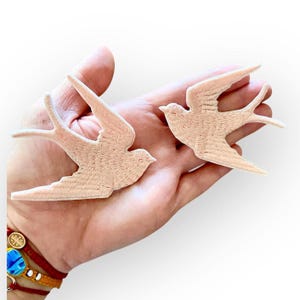 Puede incluir: Dos parches de golondrina bordados en rosa. Las aves están en vuelo con las alas extendidas.