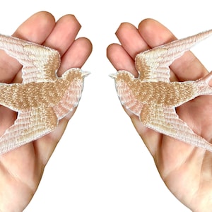 Könnte beinhalten: Zwei gestickte Bügelbilder von rosa und weißen Schwalben im Flug.