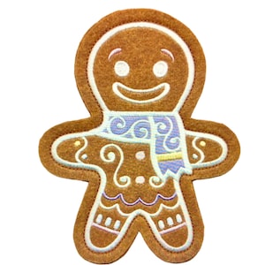 Könnte beinhalten: Ein brauner Lebkuchenmann-förmiger Aufnäher mit einem lächelnden Gesicht, weißen Augen und einem blauen Schal. Der Aufnäher hat einen weißen Rand und dekorative Wirbel. Der Lebkuchenmann ist eine festliche Weihnachtsdekoration.