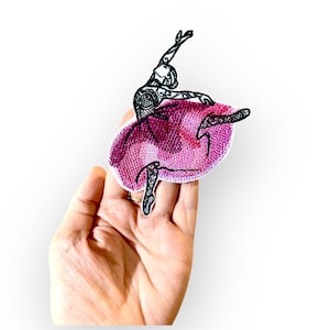 Op de afbeelding: Een geborduurde strijk-patch met een ballerina in een roze tutu. De ballerina is in de lucht, met haar armen uitgestrekt en haar benen in een sierlijke pose.
