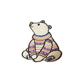 May include: White felt embroidered patch of a polar bear wearing a purple, orange, and yellow striped sweater. The bear is sitting with its head tilted up.