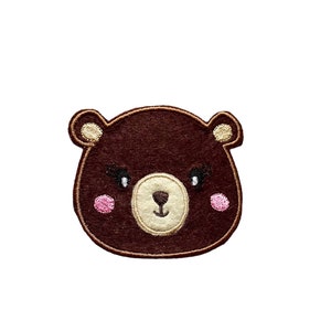 May include: Brown felt bear face with pink cheeks, black eyes, and a beige nose and mouth.