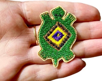 May include: Green embroidered turtle patch with a yellow, purple, and black diamond pattern in the center. The patch is on a beige background.