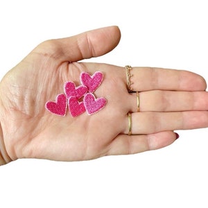 May include: Four pink felt heart patches, each with a slightly different shape, are displayed on a hand.