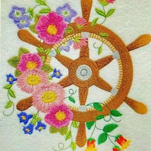 Può includere: Disegno ricamato di un timone di nave con una ghirlanda floreale di fiori rosa, gialli e blu. Il timone è marrone con un centro bianco e raggi.