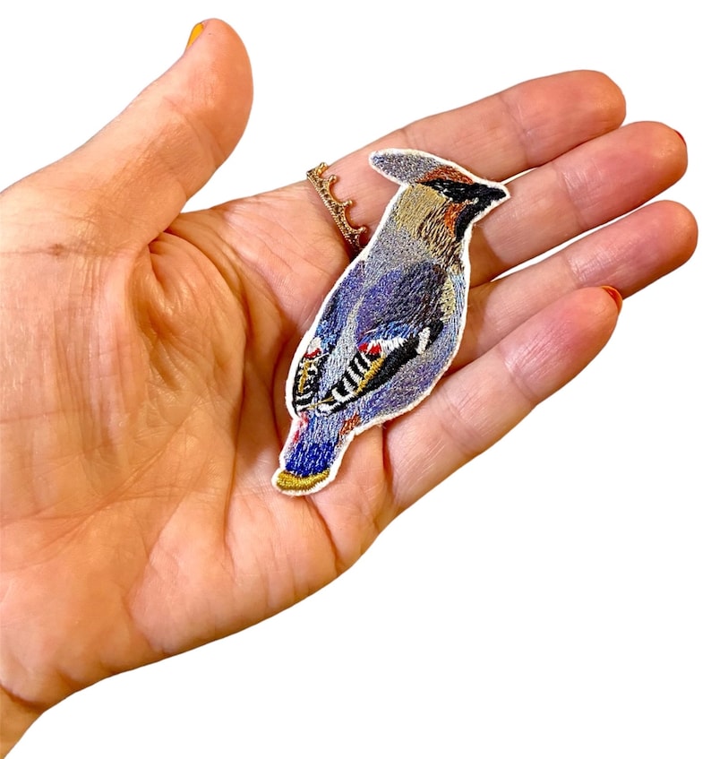 May include: A blue and brown embroidered iron-on patch of a bird with a white background.