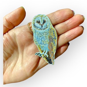 May include: A blue and gold embroidered iron-on patch of a barn owl with a white face.