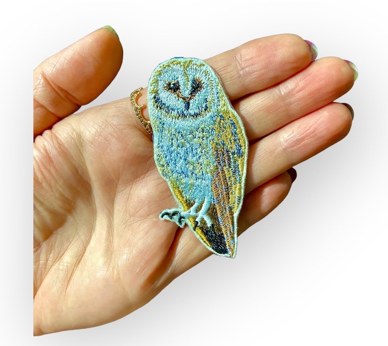 May include: A blue and gold embroidered iron-on patch of a barn owl with a white face.