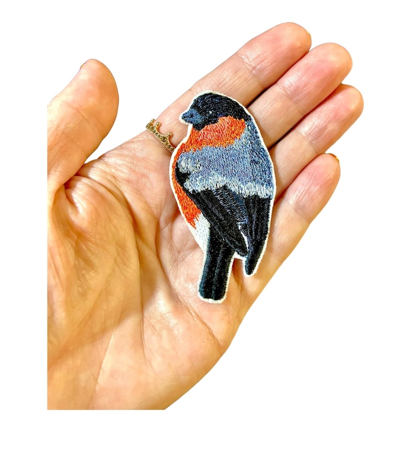 May include: Embroidered iron-on patch of a black, red, and blue bird. The bird is facing to the right and has a white belly.