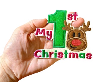Pode incluir: Patch bordado verde e vermelho com uma rena e o texto "My 1st Christmas".