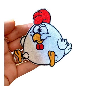 Puede incluir: Parche blanco bordado para planchar de un pollo de dibujos animados con cresta roja, patas amarillas y pico rojo. El pollo tiene una expresión divertida con los ojos cerrados y la lengua fuera.