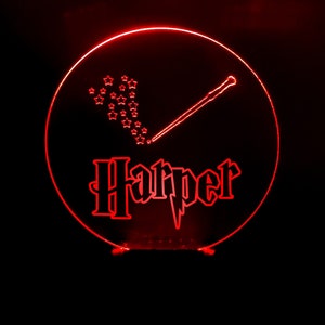 Könnte beinhalten: Rotes LED-Nachtlicht mit einem runden Design, das einen Zauberstab mit Sternen und den Namen "Harper" in einer stilisierten Schrift zeigt.