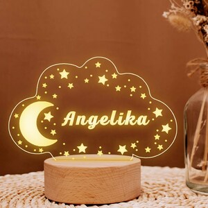 May include: A wooden night light shaped like a cloud with a crescent moon and stars. The name "Angelika" is written in the center of the cloud.