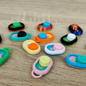 May include: Assortment of colourful camera phone grips with different designs and colours. The grips are made of plastic and have a button on the top.