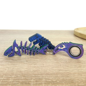 May include: A set of three colorful keychains featuring a fish skeleton, a dinosaur skeleton, and a bottle opener. The keychains are made of plastic and have a blue and purple iridescent finish.