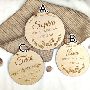 May include: Three wooden plaques with engraved text and floral designs. The plaques are labeled A, B, and C. Plaque A reads "Willkommen kleines Wunder! Sophia 15:23 Uhr 3239g 52cm 27.01.2023". Plaque B reads "Hallo Welt! Leon 09:11 Uhr 2977g 54cm 11.03.2023". Plaque C reads "Theo 19:27 Uhr 3155g 51cm 15.06.2023".