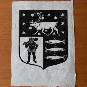 May include: Black and white print of a coat of arms on textured paper. The design includes a reindeer, stars, a figure holding a club, and three fish. The print is signed and dated.