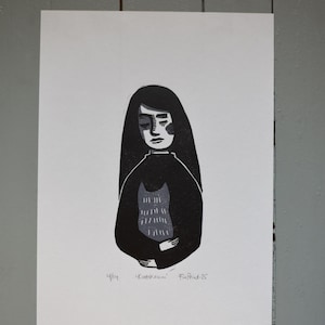 Puede incluir: Grabado en linóleo en blanco y negro de una persona con pelo largo, que lleva una parte superior oscura sobre una prenda estampada. La impresión incluye el texto "4/14 'Kattkraw' FinPrint-25". La obra de arte tiene un estilo minimalista.