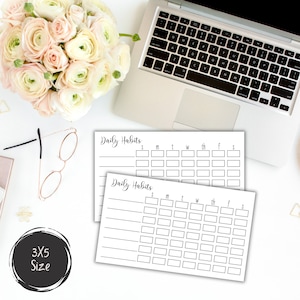 May include: Two white 3x5 inch Daily Habits tracker cards with a black font, next to a laptop, glasses, and a bouquet of flowers. The cards have boxes for tracking daily activities.