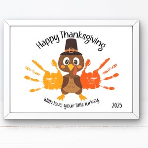 May include: A framed print with a Thanksgiving theme. The artwork features a cartoon turkey with handprint feathers in orange and yellow. The text reads "Happy Thanksgiving" and "With love, your little turkey" with the year 2025.