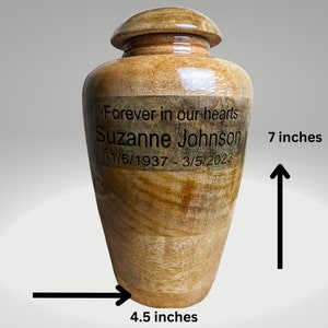 Pu&ograve; includere: Un'urna in legno con coperchio, con l'iscrizione "Forever in our hearts" e il nome "Suzanne Johnson" con le date. L'urna &egrave; alta circa 17.8 cm e larga 11.4 cm, con venature del legno marrone chiaro.
