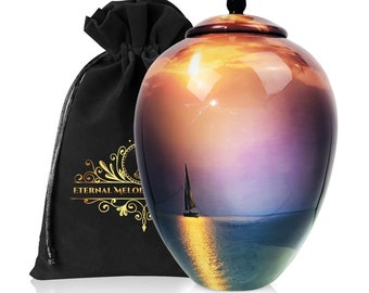 May include: A ceramic urn with a sunset and sailboat design. The urn is a light brown color with a glossy finish. The urn is sitting on a white surface. The urn is accompanied by a black velvet bag.