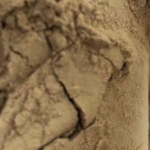 May include: Close-up of a light brown powder with a rough, textured surface. The powder is piled high and has a slightly grainy appearance.