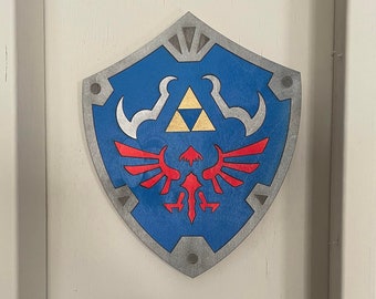 May include: A blue and silver shield with a red and yellow winged symbol in the centre. The shield is a popular symbol from the Legend of Zelda video game series.