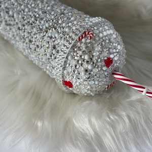May include: A white tumbler covered in rhinestones with a red and white candy cane straw.