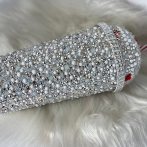 May include: A white tumbler covered in silver and white rhinestones with a red and white striped straw.
