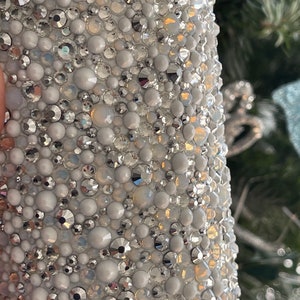 May include: A close-up of a white surface covered in small, iridescent rhinestones. The rhinestones are arranged in a random pattern and create a sparkling effect.