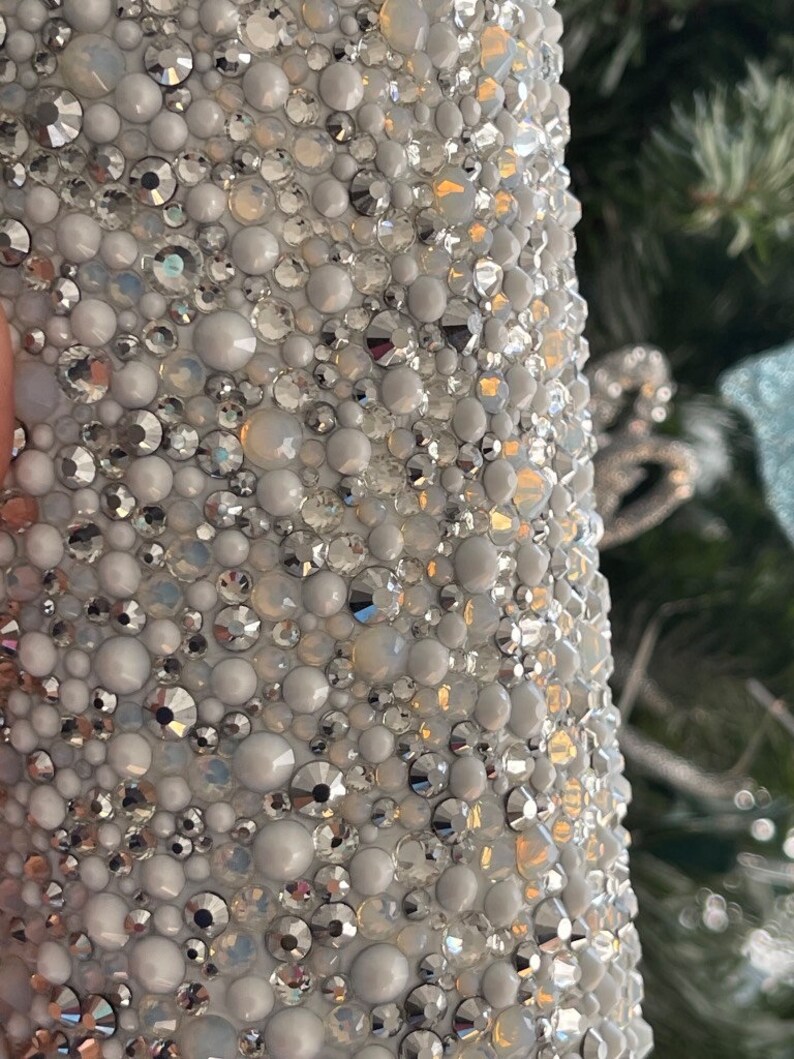 May include: A close-up of a white surface covered in small, iridescent rhinestones. The rhinestones are arranged in a random pattern and create a sparkling effect.