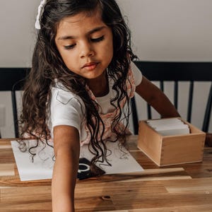 Children 2-6 years old is reach out to pick up her alphabet cards on a wooden table.