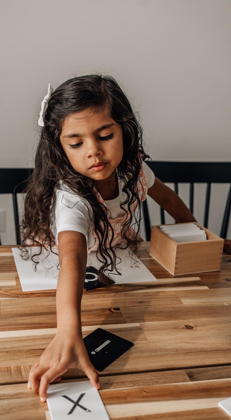 Children 2-6 years old is reach out to pick up her alphabet cards on a wooden table.