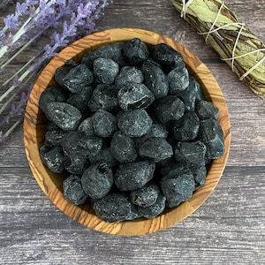 May include: A bowl filled with black obsidian stones. The bowl is made of wood and has a natural grain pattern. The stones are smooth and have a glossy finish.