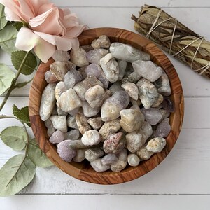 May include: A wooden bowl filled with a variety of white, gray, and pink tumbled stones. The stones are smooth and have a natural, polished look.