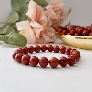 May include: A red gemstone bracelet made of round beads. The bracelet is on a white surface.