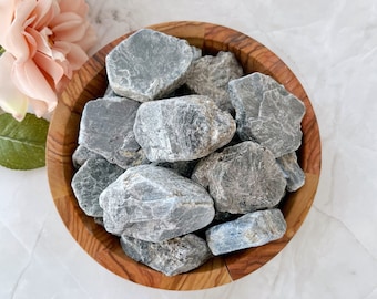 May include: A wooden bowl filled with a collection of gray and blue kyanite crystal rough stones.