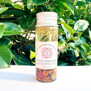 May include: A small glass bottle with a white lid filled with a clear liquid and herbs. The label reads "The Stone Sanctuary Metaphysical Gifts Root Chakra Oil Use: Balance, Centering, Confidence, Courage, Grounding, Strength, Vitality 15 ml | 1/2 oz"