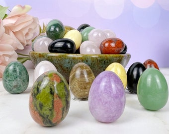 Puede incluir: Una colección de huevos de piedras preciosas pulidas en varios colores, incluyendo verde, rosa, rojo, negro y blanco, exhibidos en un cuenco. Los huevos son lisos y tienen un acabado natural y pulido.