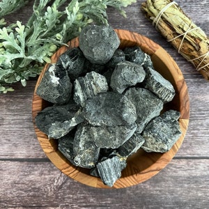 May include: A wooden bowl filled with black tourmaline rough crystals. The crystals are various sizes and shapes, with some having a striated appearance.